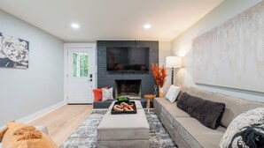 A modern living room with a fireplace, a sofa, a coffee table, and a TV mounted on the wall. - Modern Blacksburg retreat near VT, Radford & scenic Claytor Lake Perfect for work, play & relaxation (Blacksburg)