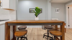 A modern kitchen with a wooden table and bar stools, a potted plant, and a wall-mounted sign that reads "EAT". - Modern Blacksburg retreat near VT, Radford & scenic Claytor Lake Perfect for work, play & relaxation (Blacksburg)