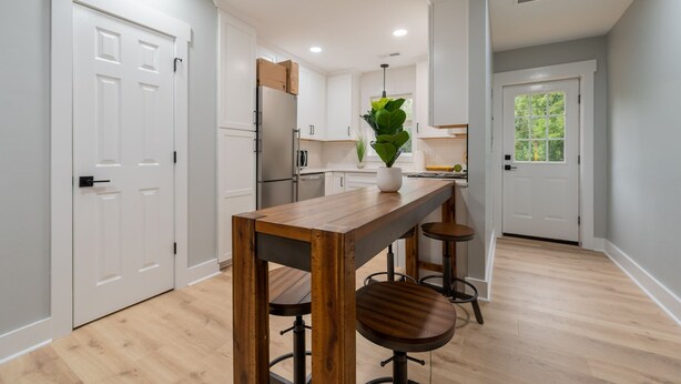A modern kitchen with white cabinets, a wooden table, and bar stools.