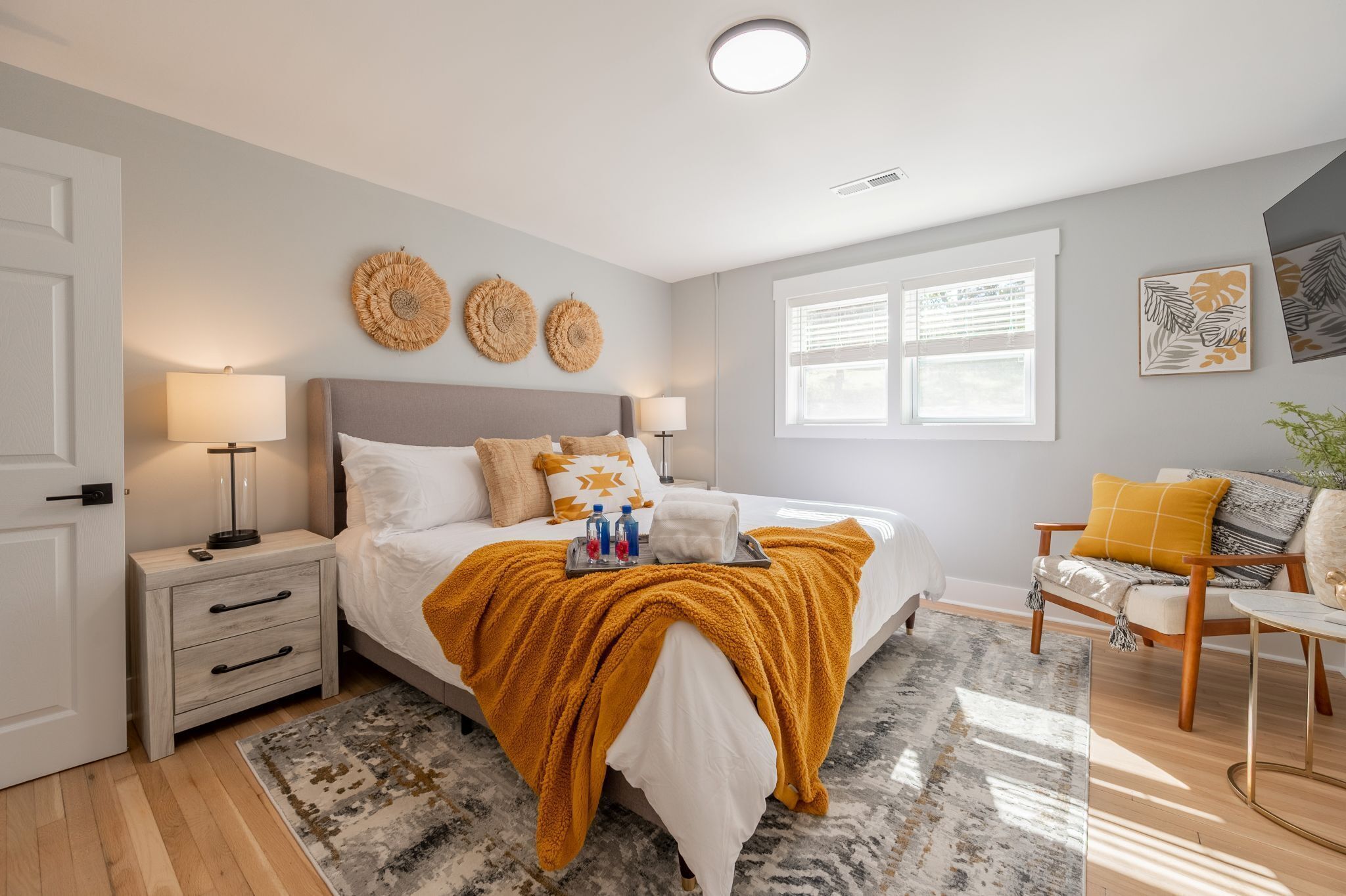 A bedroom with a bed, bedside tables, a nightstand, a chair, a window, and wall art.