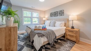 A modern bedroom with a bed, bedside tables, a nightstand, a large window, and a potted plant.