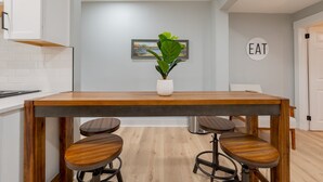 A modern kitchen with a wooden table, bar stools, a potted plant, and a wall-mounted sign that says "EAT".