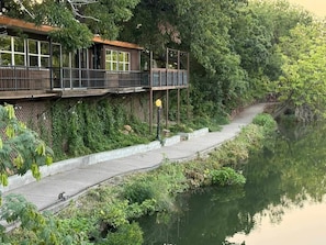 Une promenade au bord de la rivière, avec une terrasse en bois et un sentier pavé de pierres.