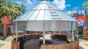 A gazebo with a metal roof and stone base, surrounded by outdoor seating and barbecue grills.