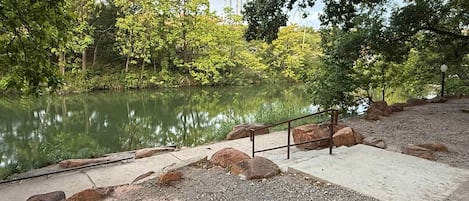 Un parc paisible avec un étang, une allée en béton et une rambarde en métal.