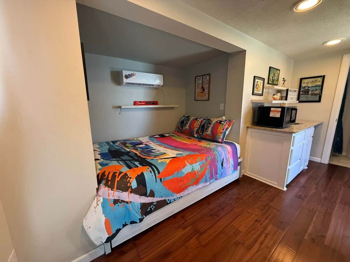 A bedroom with a bed, a small kitchenette, and a ceiling fan.