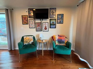 Una habitación con dos sillones verdes, una mesita redonda y un televisor montado en la pared.