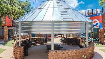 Un espace extérieur abrité, doté de murs en pierre et d’un toit en métal, entouré de mobilier de jardin et d’un bâtiment voisin portant l’enseigne « Gulf ».