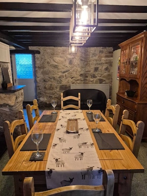 A dining area with a wooden table, chairs, a stone wall, and a cabinet with glass doors.