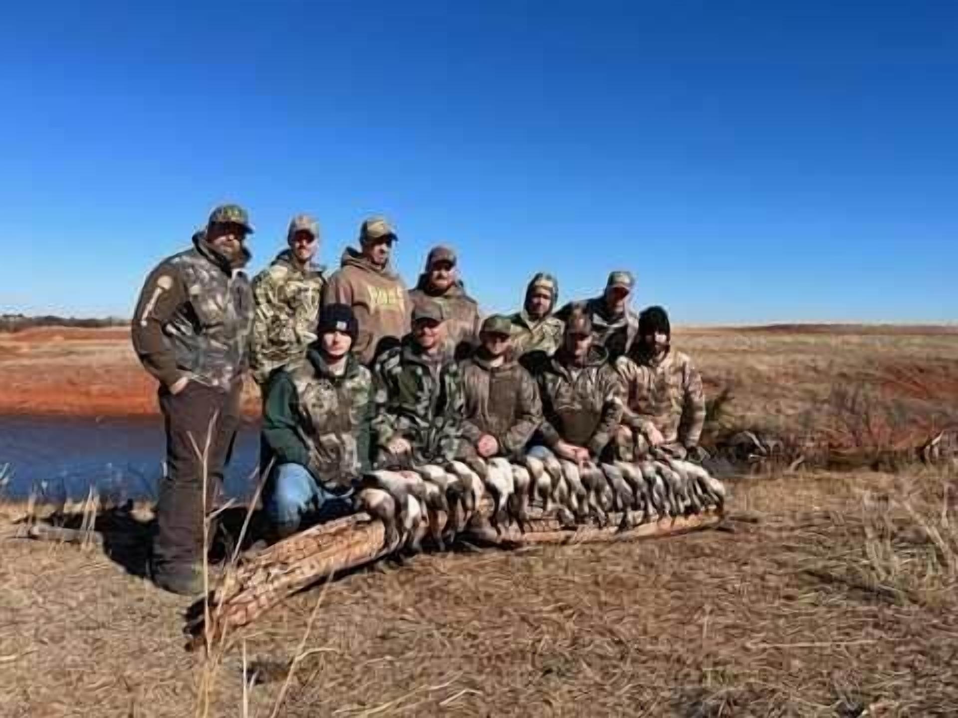 Un groupe de personnes, vêtues pour les activités de plein air, posent avec un tronc d’arbre et des poissons, ce qui laisse supposer qu’elles pratiquent la chasse ou la pêche.