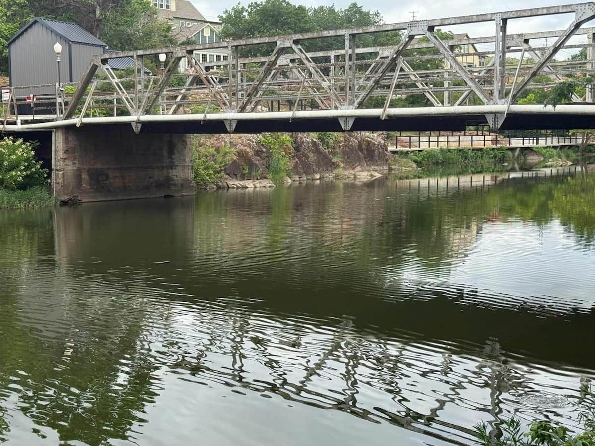 Eine Brücke über einem ruhigen Fluss, links davon ein kleines Gebäude.