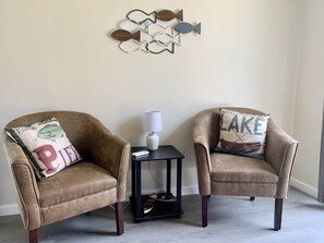 Two armchairs with decorative pillows, a small table with a lamp, and a wall-mounted fish decoration.