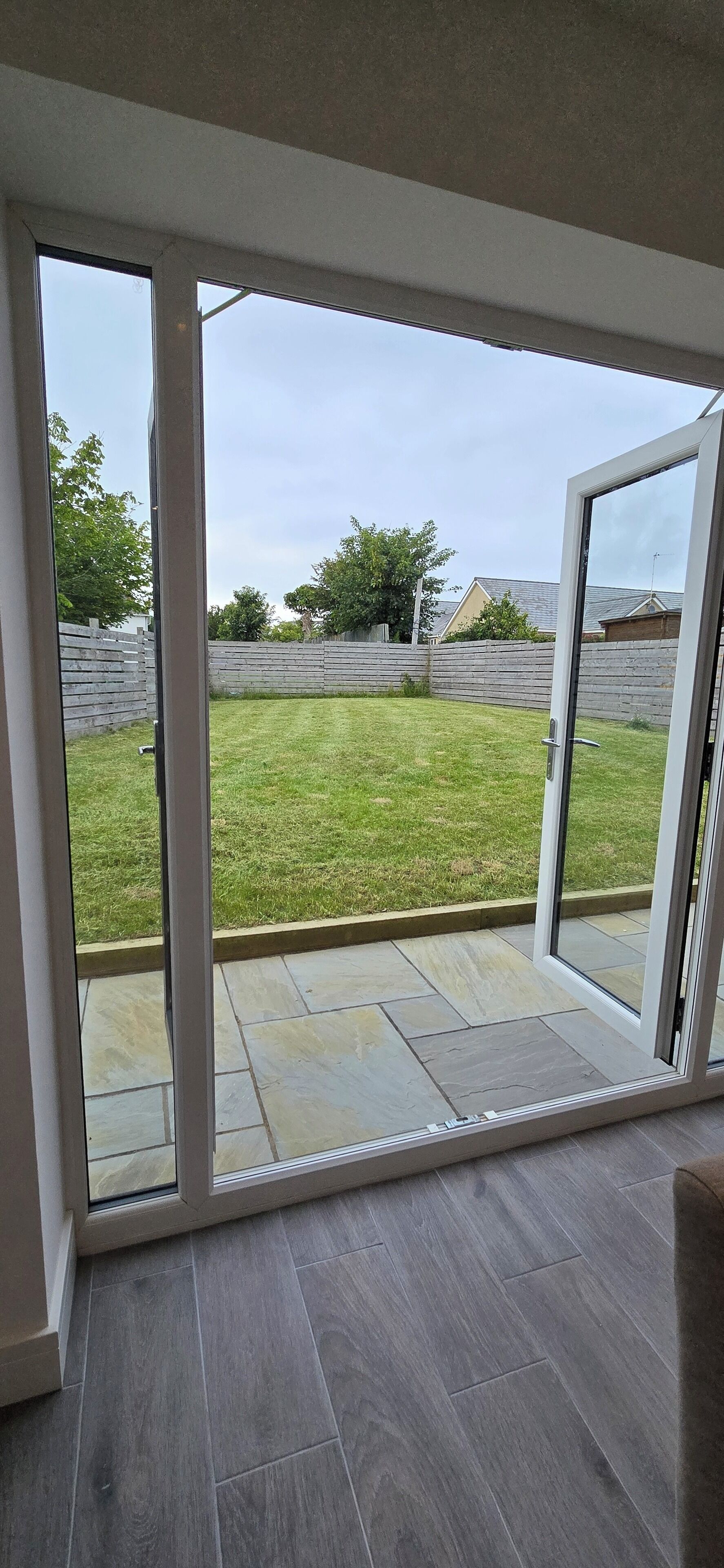 A room with a large sliding glass door leading to a backyard with a wooden fence and a grassy lawn.