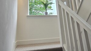 A staircase with a textured carpet, a white railing, and a window with a plant.