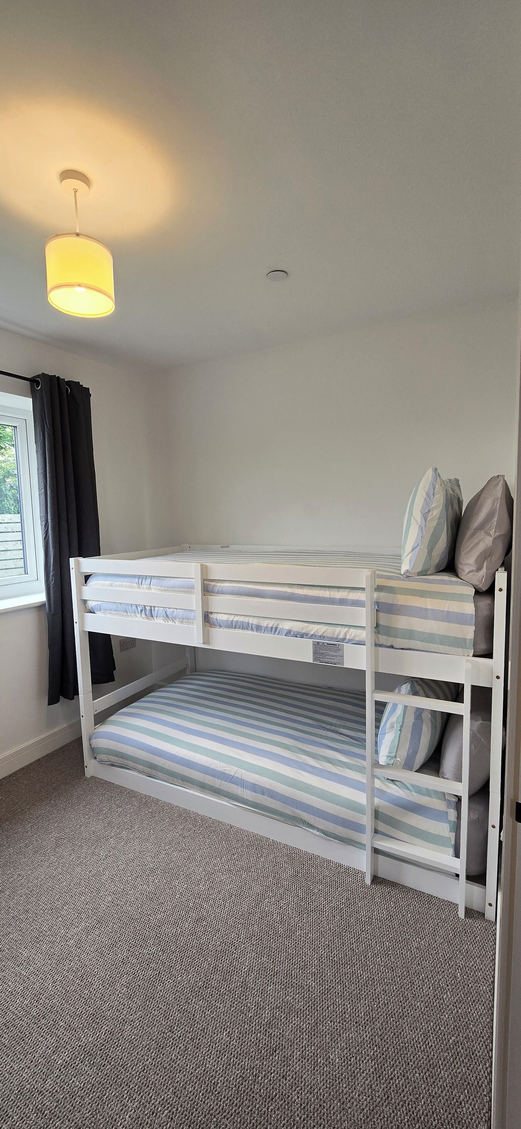 A bunk bed room with a window, curtains, and a hanging light fixture.