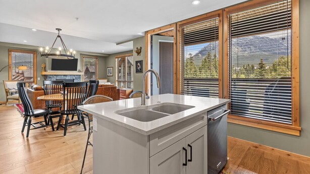 Una cocina moderna con una isla central, piso de madera y grandes ventanales con persianas.