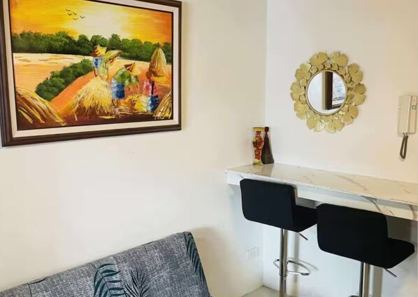Ein Zimmer mit einem Gemälde einer ländlichen Szene, einem weißen Schreibtisch mit Spiegel und einem grauen Sofa.