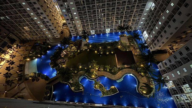 A high-rise hotel with a central swimming pool surrounded by lush greenery and palm trees. - Metro’s Hideaway Shore Tower B (Pasay City)