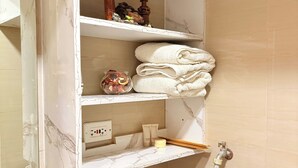 A bathroom with a marble vanity, a towel rack, a small shelf with toiletries, and a black heater. - Metro’s Hideaway Shore Tower B (Pasay City)