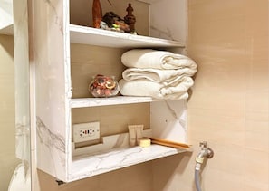 Ein Badezimmer-Waschtisch mit Marmorplatte, ein Ablagefach mit gefalteten Handtüchern, eine Badezusatz-Glase und ein Seifenspender.
