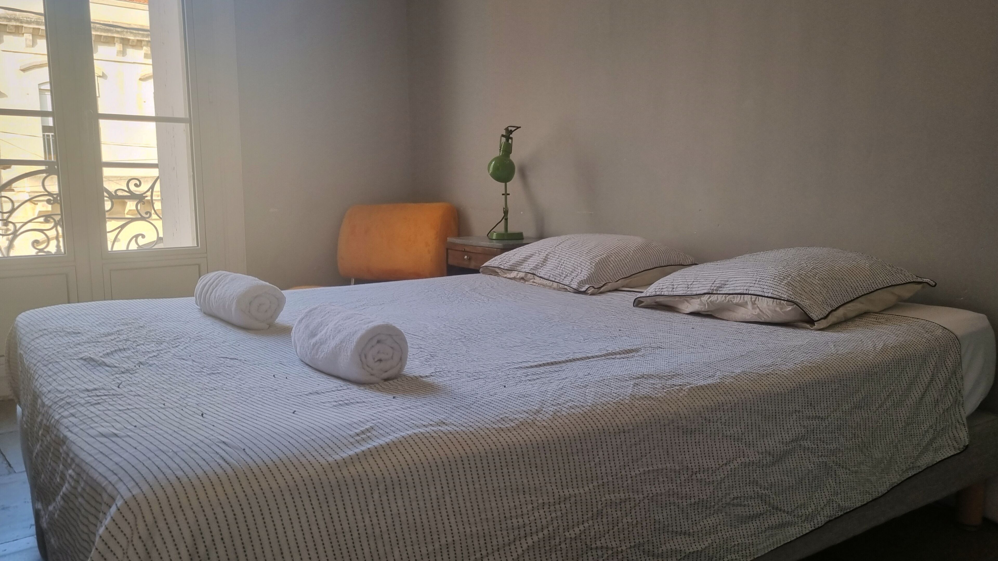 A neatly made bed with a patterned bedspread, two pillows, and two rolled towels.