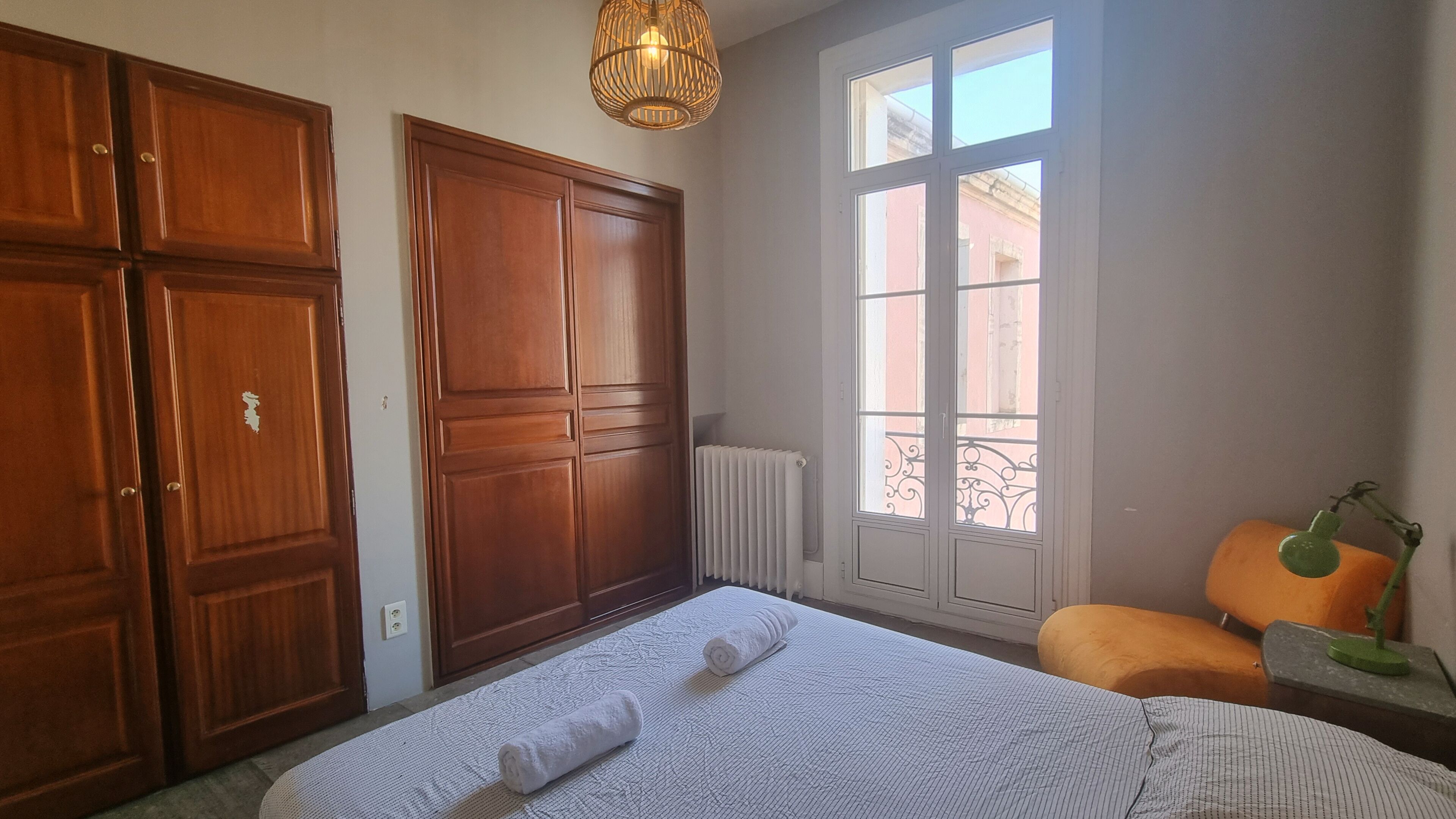 Een slaapkamer met een groot bed, een houten garderobe en een raam met uitzicht op gebouwen.