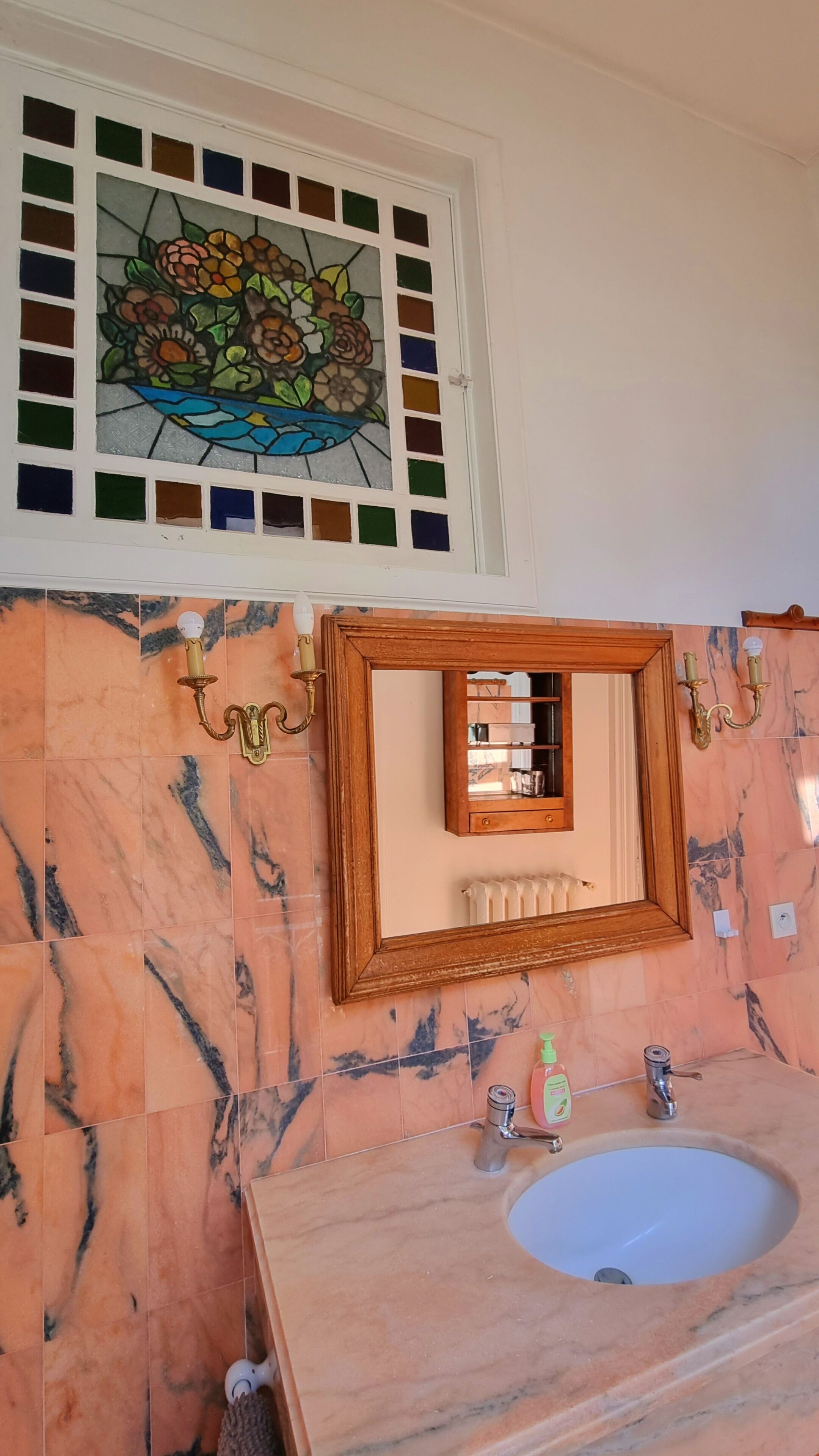 A bathroom with a marble sink, a mirror with a wooden frame, and a stained glass window above the mirror.