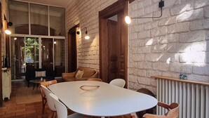 A dining area with a white table and wooden chairs, a brick floor, and a white brick wall. - Villa Muscat, authentic charm in the heart of town / beaches 3 kilometers (Frontignan)