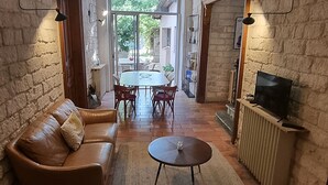 A living room with a sofa, a coffee table, and a TV stand. There is a dining area with a table and chairs in the background. - Villa Muscat, authentic charm in the heart of town / beaches 3 kilometers (Frontignan)