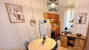 Une cuisine compacte avec des meubles en bois, un four à micro-ondes et un petit réfrigérateur. On y trouve une table à manger avec des chaises et une petite décoration de Noël.