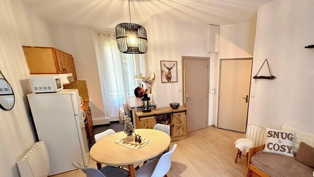 Un espace de vie compact comprenant un coin repas, une kitchenette et un coin salon confortable agrémenté d’un coussin douillet.