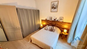 Une chambre à coucher avec une tête de lit en bois, un lit recouvert d’une courtepointe, deux lampes de chevet, une porte et un rideau.