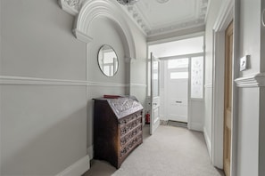A hallway with a dark wooden dresser, a round mirror, and a white door at the end.