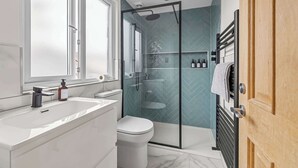 Un baño moderno con ducha de vidrio, un lavamanos blanco y un inodoro.