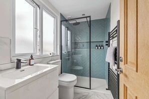 Un baño moderno con ducha de vidrio, un lavamanos blanco y un inodoro.