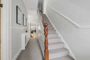 A hallway with a staircase, white walls, and framed artwork.