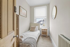 A small bedroom with a bed, a bedside table, a window, a mirror, and a door.
