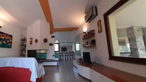 A room with a bed, a desk, a TV, a kitchen area, and a dining area with bar stools. - House in the green between sea and countryside (San Vero Milis)