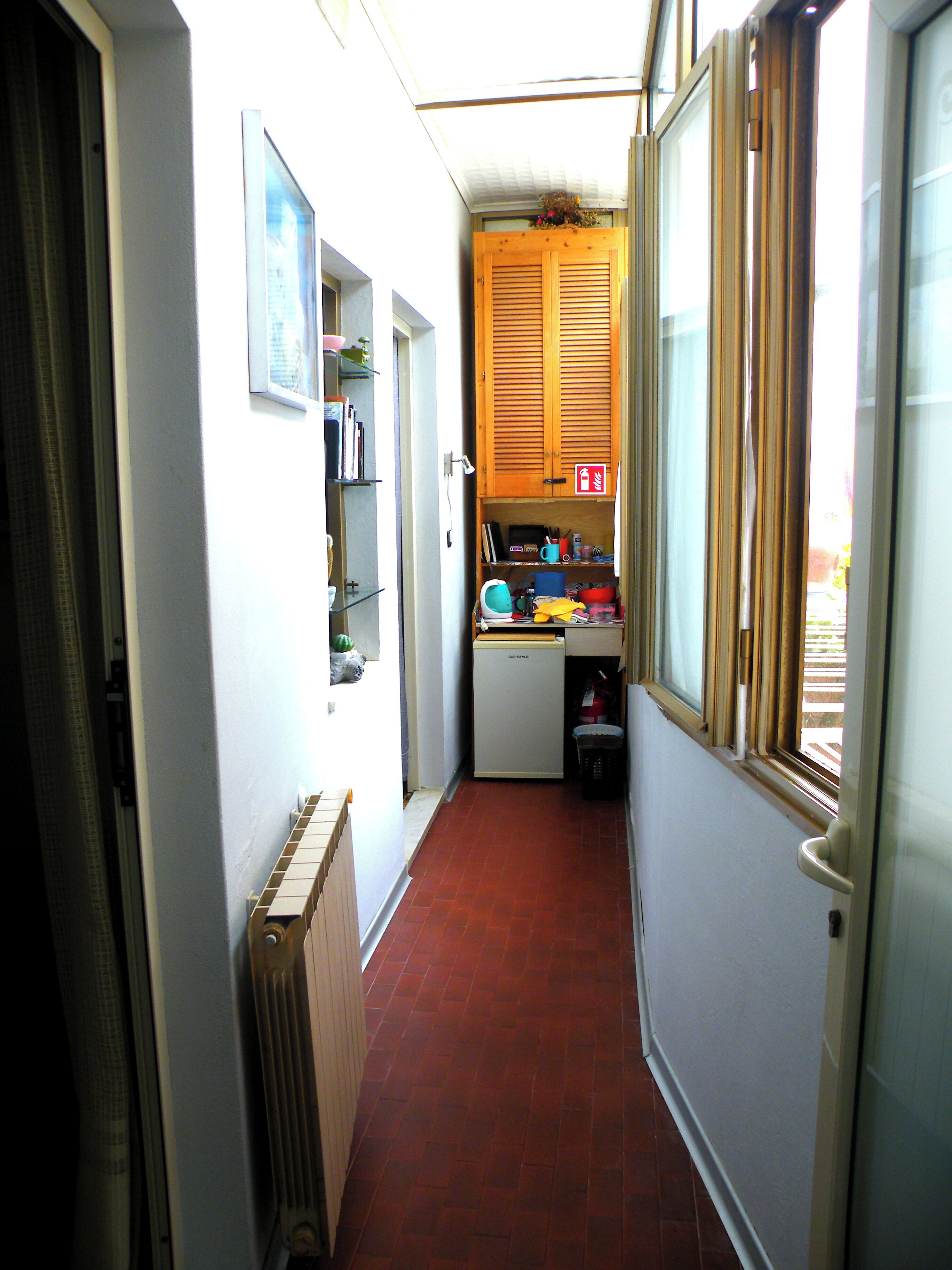 Un couloir étroit avec un radiateur, une petite cuisine équipée avec des meubles en bois et une fenêtre avec des stores.