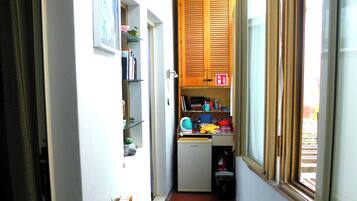 Un couloir étroit avec un radiateur, une petite cuisine équipée avec des meubles en bois et une fenêtre avec des stores.