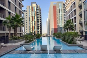A modern apartment building with a central swimming pool, surrounded by palm trees and lounge chairs.