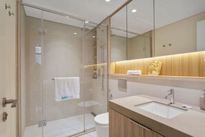 A modern bathroom with a glass-enclosed shower, a white sink, and a wooden vanity.
