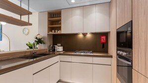 A modern kitchen with light wood cabinets, a stainless steel sink, and built-in appliances including a microwave and oven.
