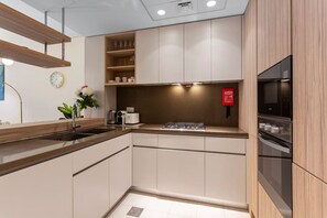 A modern kitchen with light wood cabinets, a stainless steel sink, and built-in appliances including a microwave and oven. - Art-Inspired 1 Bedroom in Wilton Terraces (Dubai)