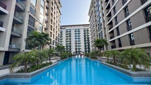 A modern hotel with a central swimming pool surrounded by palm trees and high-rise buildings.
