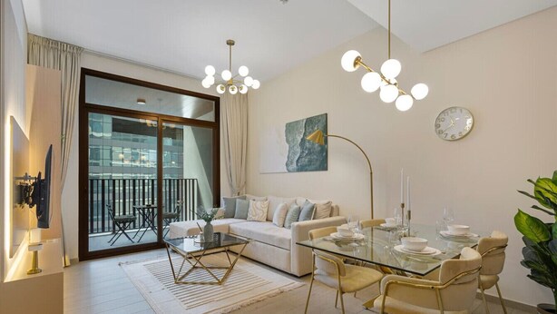 A modern living room with a glass dining table, beige sofa, and a balcony with outdoor seating.