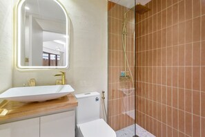 A modern bathroom with a white sink, gold fixtures, and a glass shower enclosure.