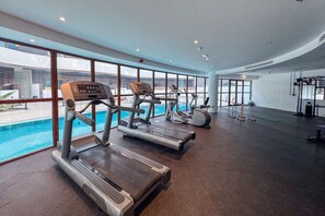 A gym with treadmills and exercise equipment, large windows overlooking a swimming pool.