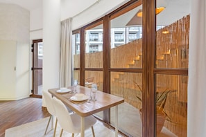 A dining area with a wooden table set for four, white chairs, and a large window with a view of buildings.