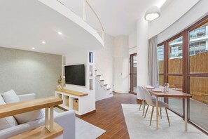 A modern living room with a flat-screen TV, wooden furniture, a staircase, and large windows.